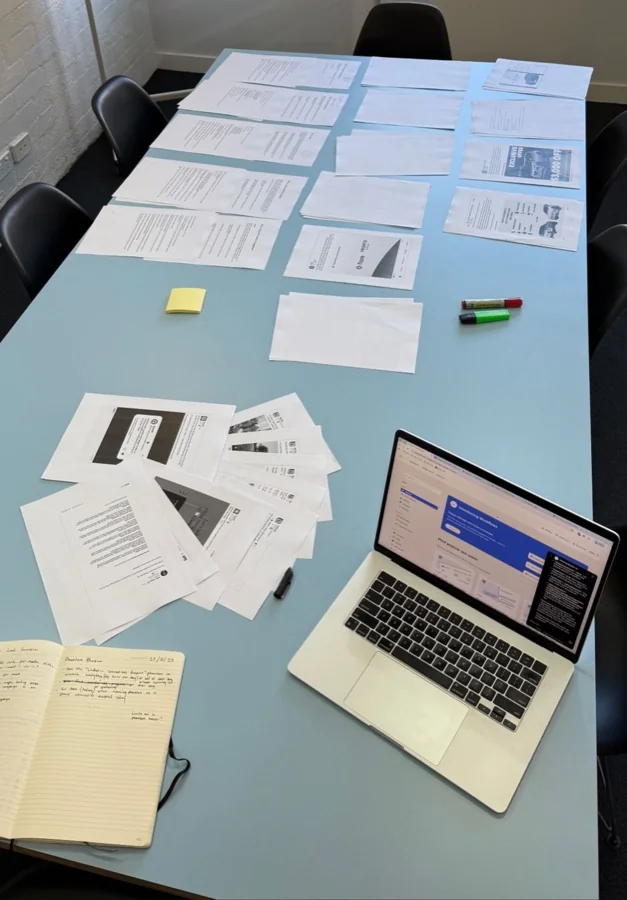 Printed pages and a laptop spread across a table in the agency office.