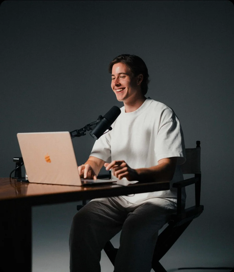 Remy smiling at his desk, working on a laptop beside a podcast microphone